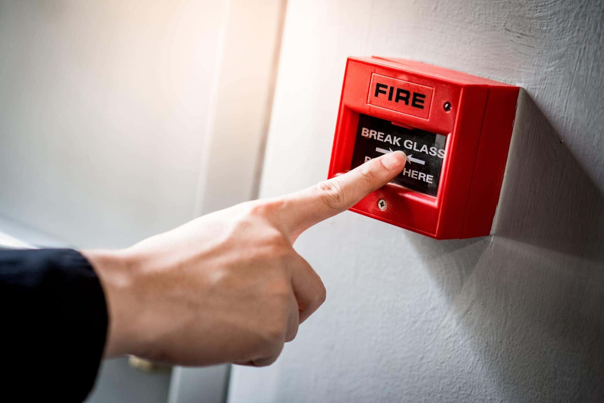 Hand reaching for a red break glass fire alarm call point